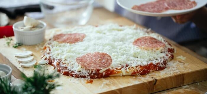 homemade pepperoni pizza being assembled with fresh dough, mozzarella cheese, and large pepperoni